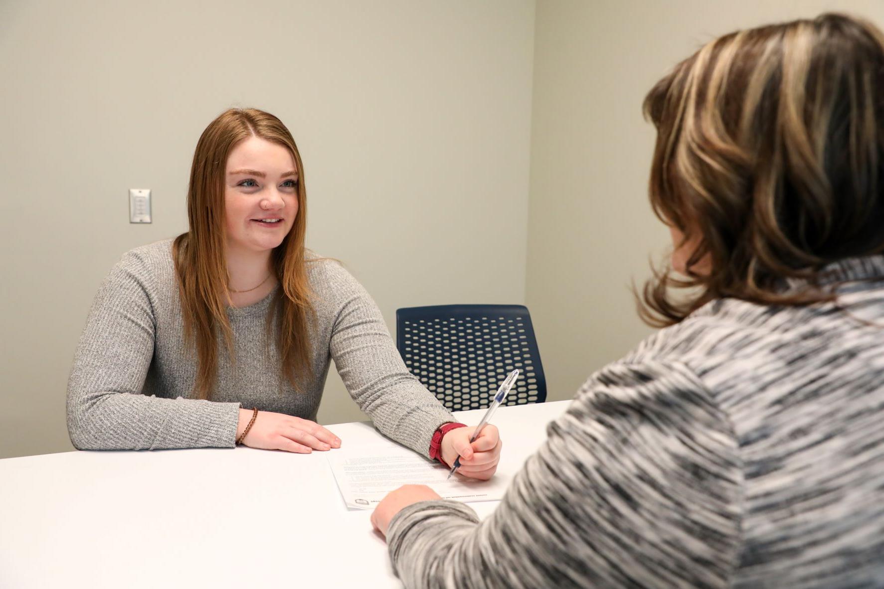 Female student sitting at a desk about to sign a document.